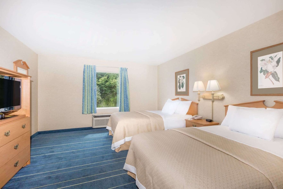 Habitación de hotel con dos camas, televisión, cómoda y ventana con cortinas.