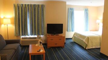 A hotel room with a sofa, a TV on a wooden stand, a small table with a remote control, and a bed with a green bedspread.