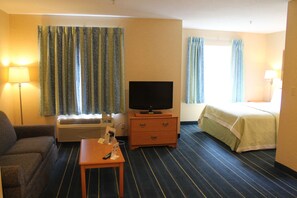 Une chambre d’hôtel avec un canapé, un téléviseur posé sur un meuble en bois, une petite table avec une télécommande et un lit recouvert d’une couverture verte.