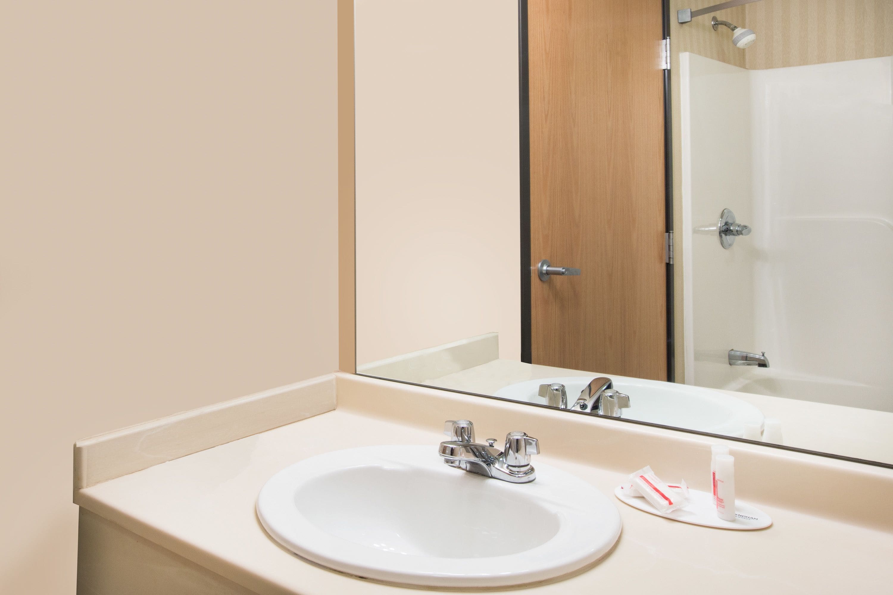 A bathroom with a white sink, a mirror, and a shower visible in the reflection.