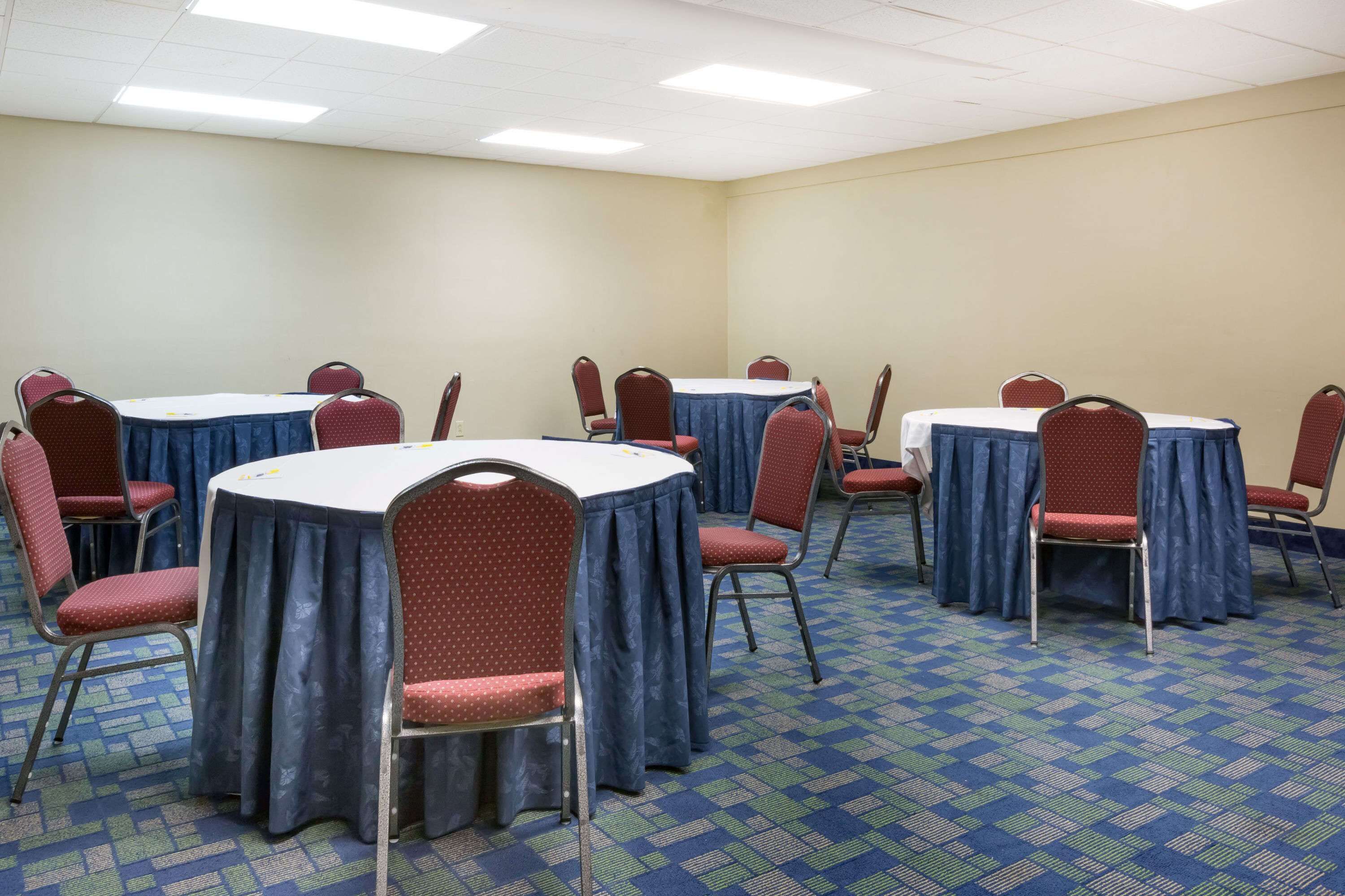 A conference room with round tables and red chairs, carpeted floor, and plain walls.