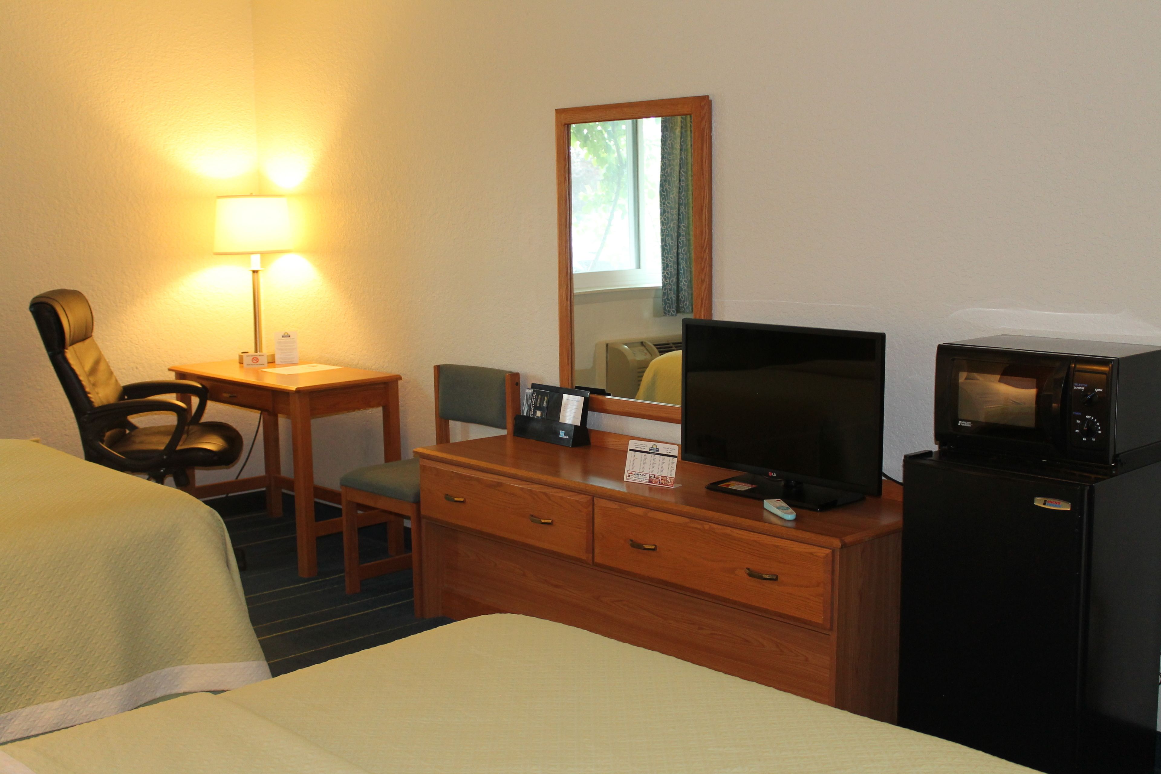 A hotel room with a bed, a desk with a lamp, a television, a refrigerator, and a mirror.