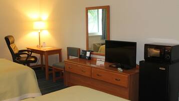 Habitación de hotel con cama, escritorio con lámpara, televisión, refrigerador y espejo.