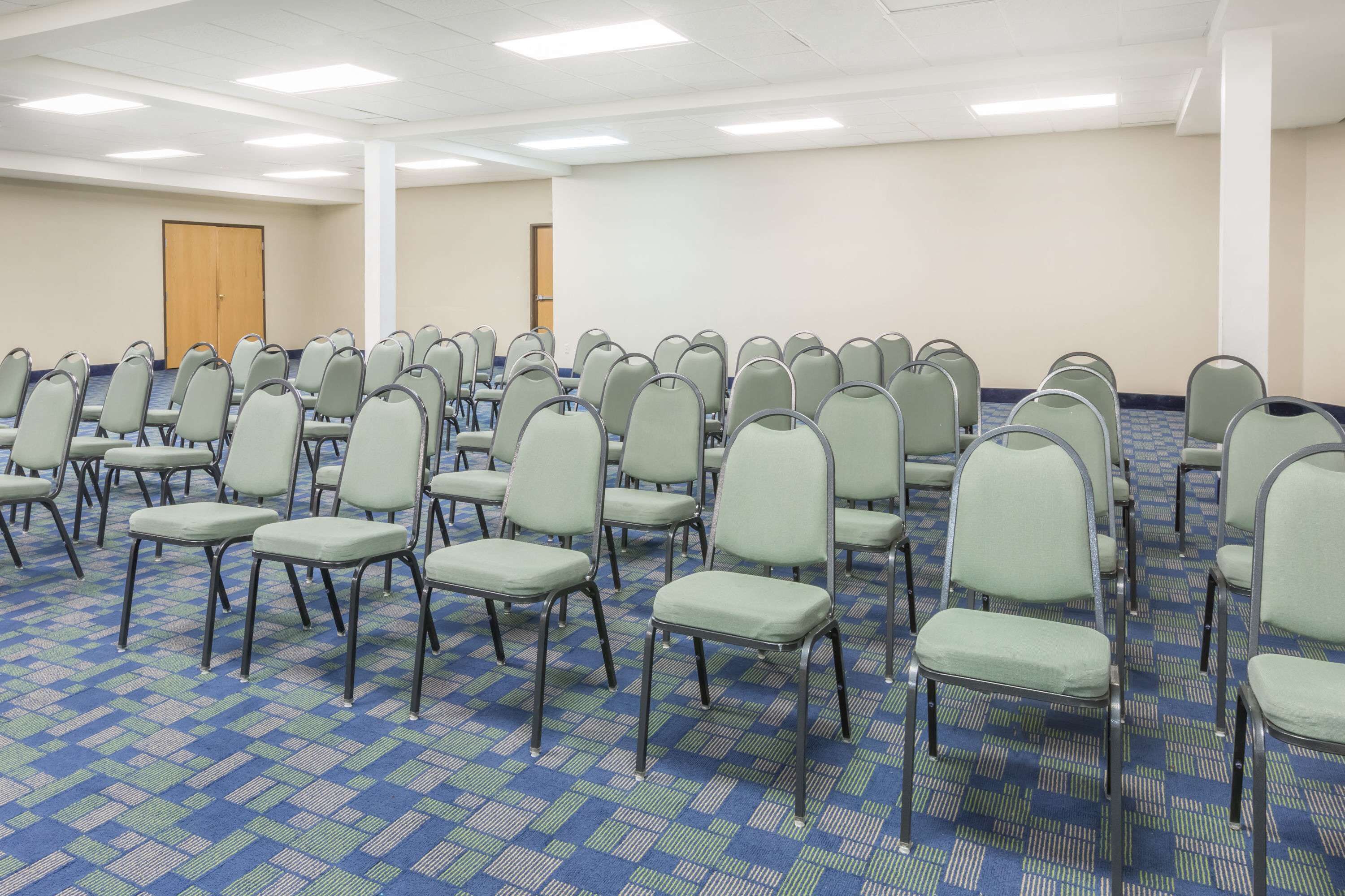 A conference room with rows of chairs, a carpeted floor, and a projector screen.