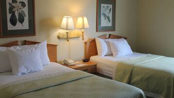 Een hotelkamer met twee bedden, een nachtkastje met een telefoon en lamp, en botanische prints in lijsten aan de wanden.