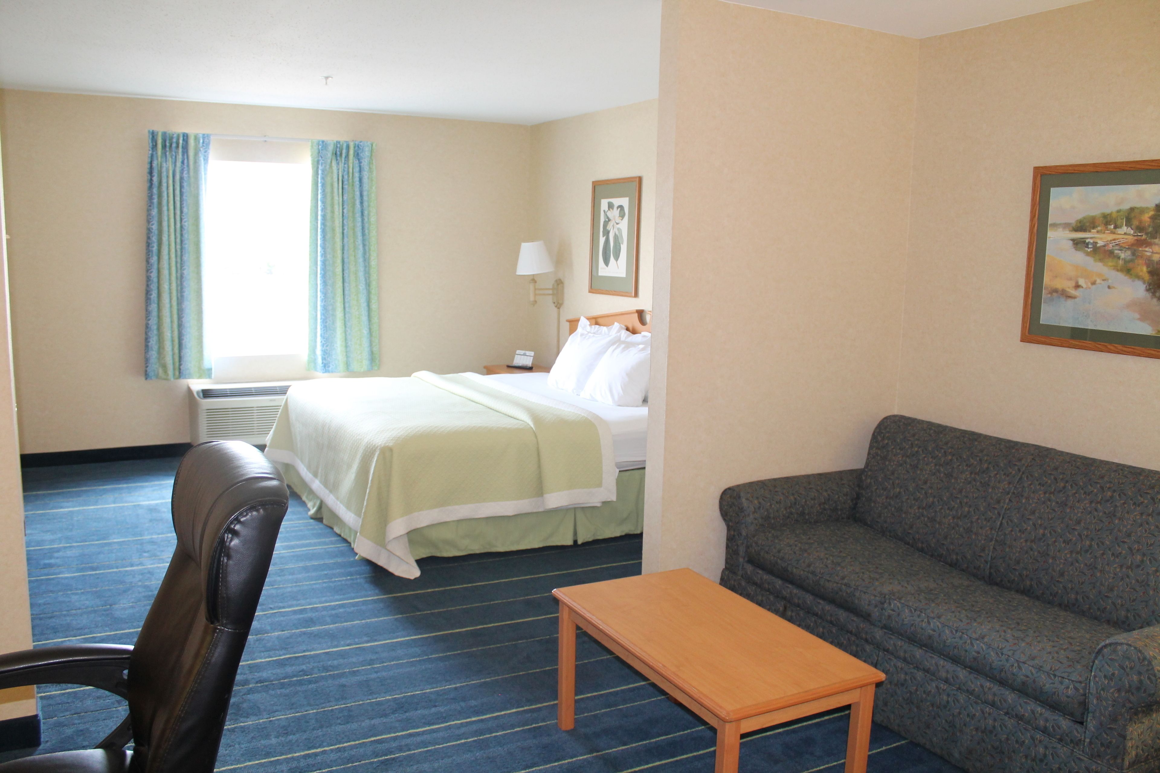 A hotel room with a bed, a sofa, a wooden table, and a chair.