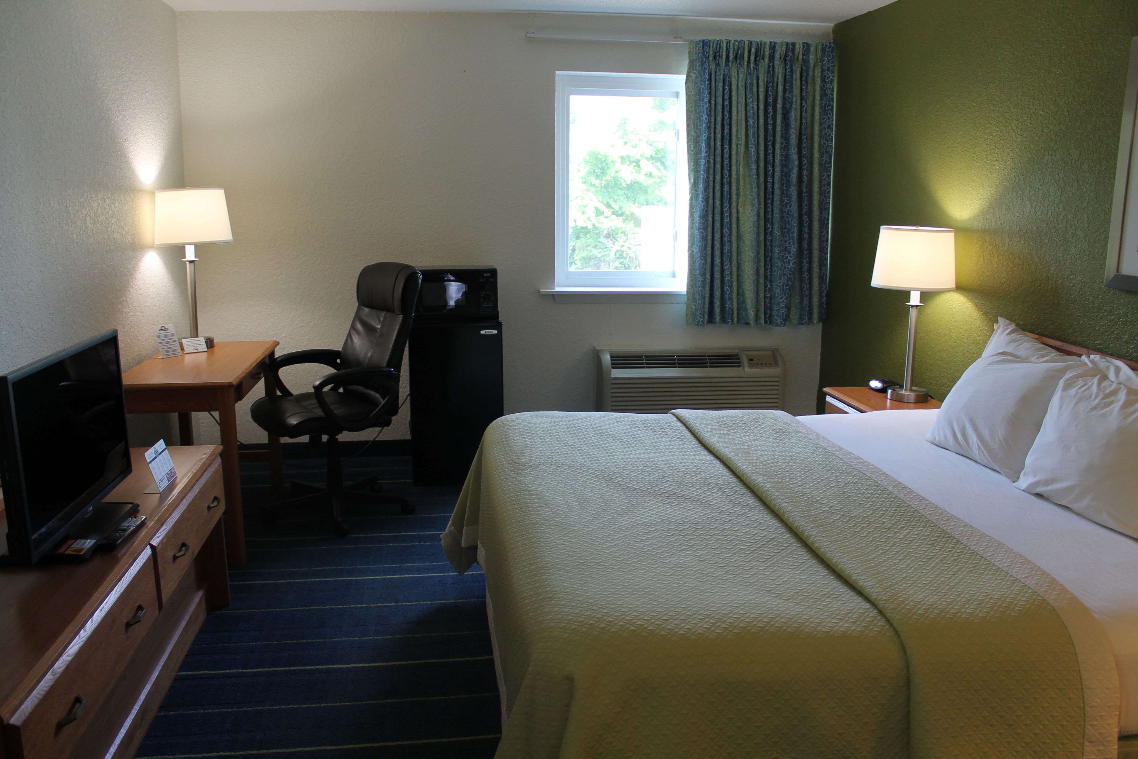 A hotel room with a bed, desk, chair, television, and a window with curtains.