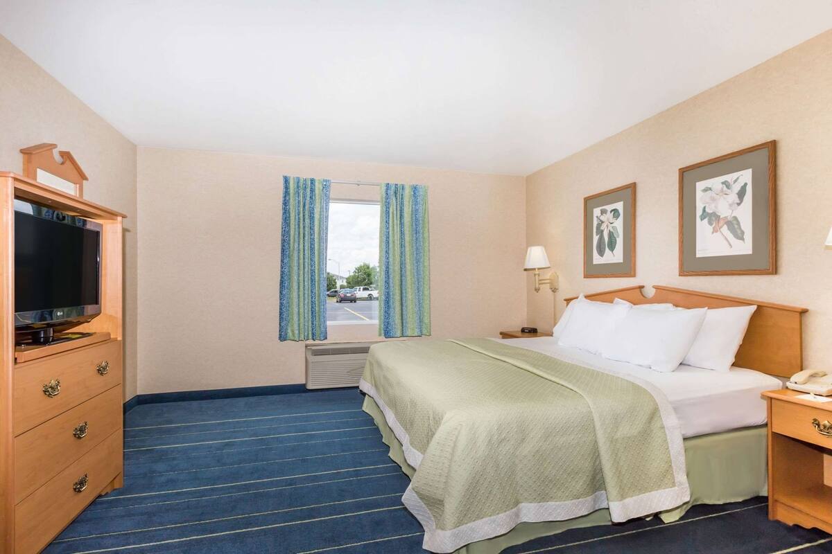 A hotel room with a bed, a TV, a desk, a lamp, and a window with curtains.