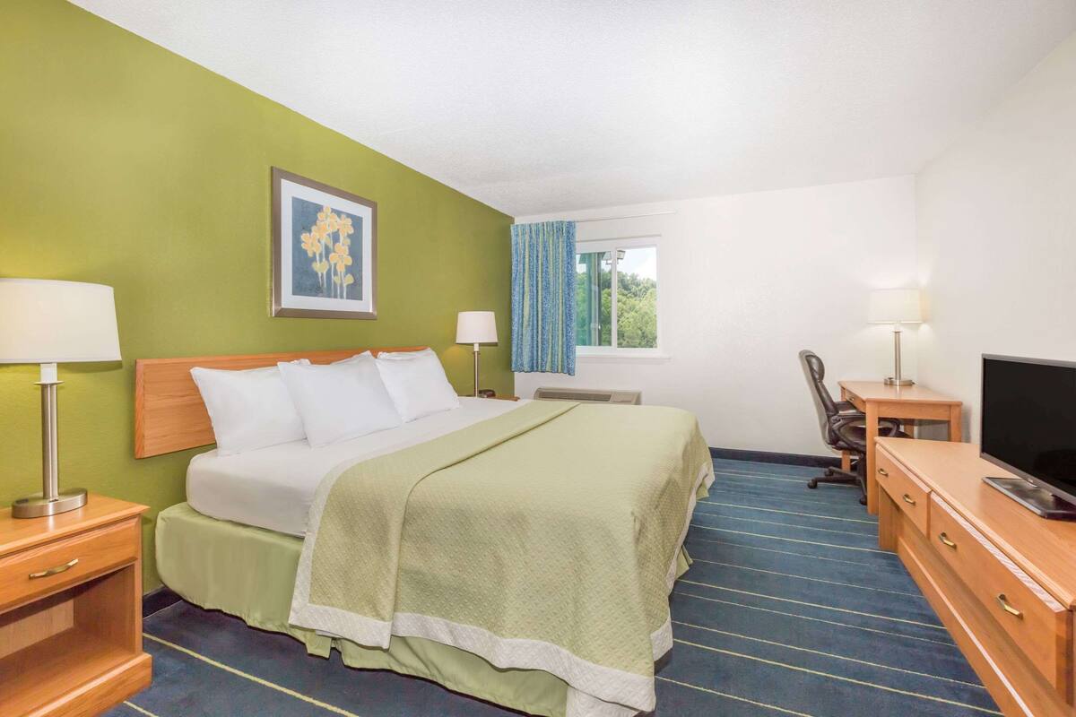 A hotel room with a bed, a desk, a television, and a window with curtains.