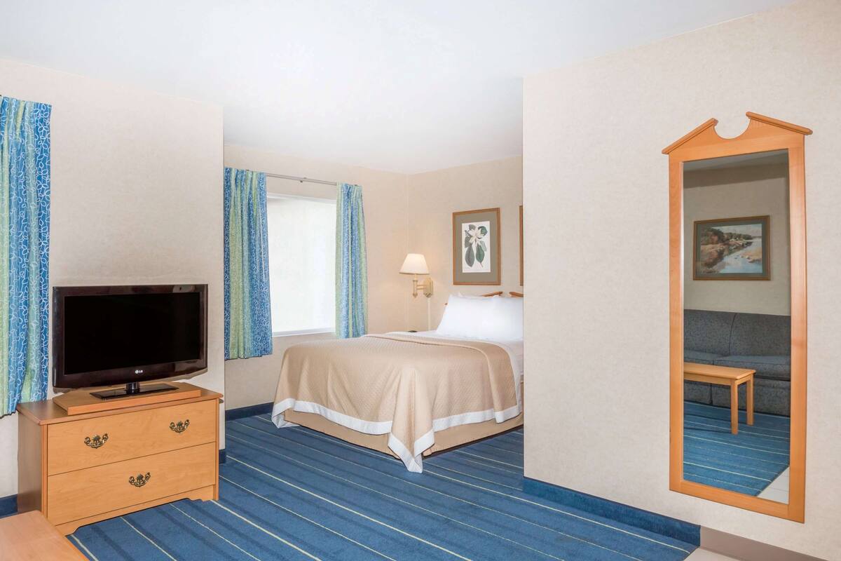 A hotel room with a bed, a TV on a wooden dresser, a desk, and a mirror.