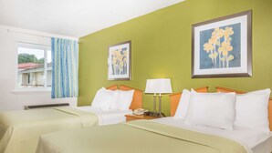 Hotelkamer met twee bedden, een raam met gordijnen, een muur met twee ingelijste foto’s en een nachtkastje met lamp en telefoon.