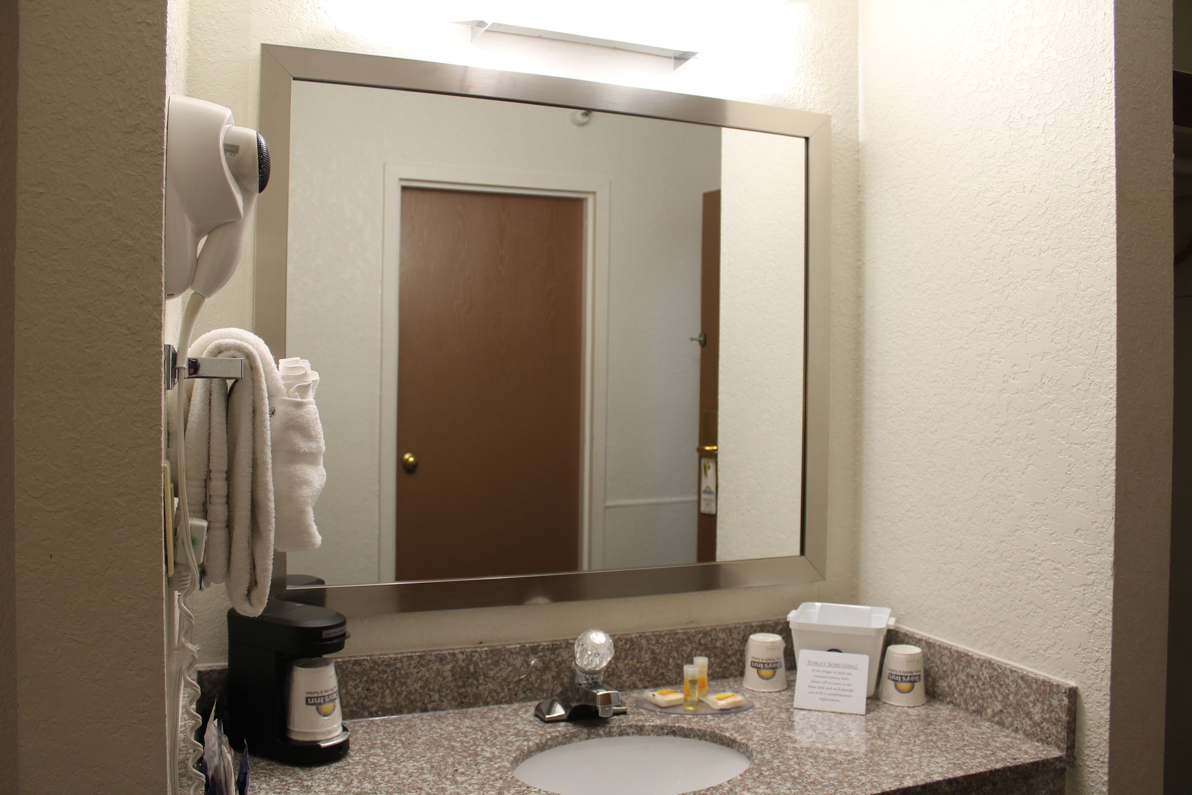 A hotel bathroom with a sink, mirror, towel rack, and toiletries.