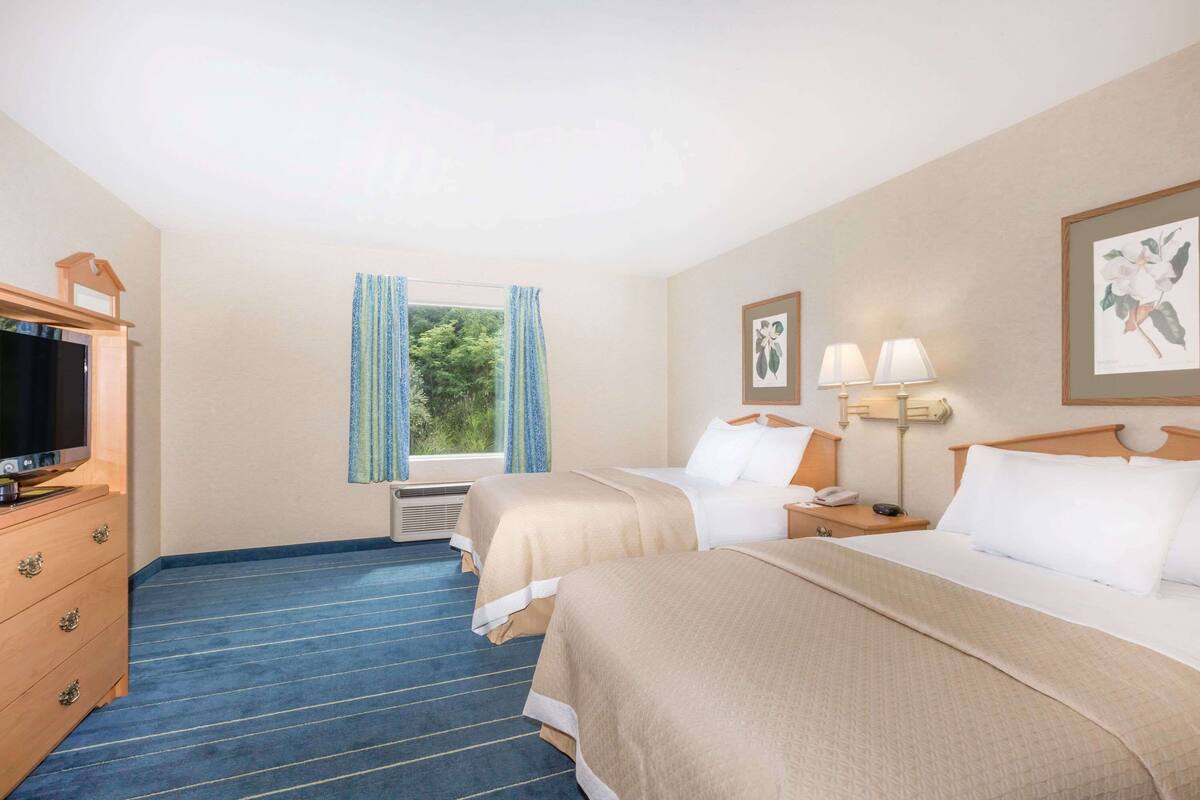 A hotel room with two beds, a TV, a dresser, and a window with curtains.