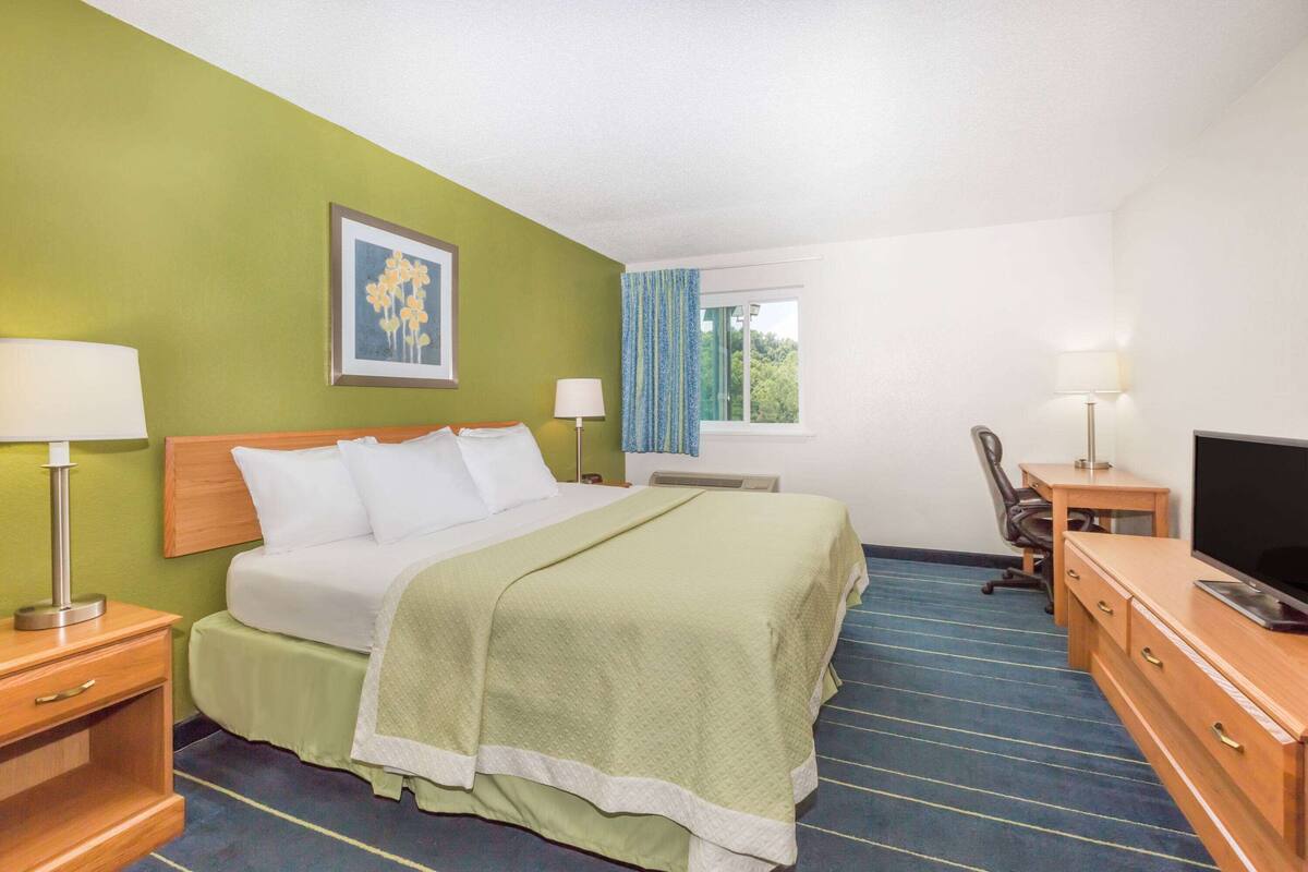 A hotel room with a bed, a desk, a chair, a television, and a window with curtains.