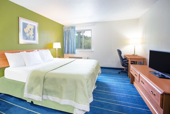Habitación de hotel con cama, escritorio, silla, televisor y ventana con cortinas.