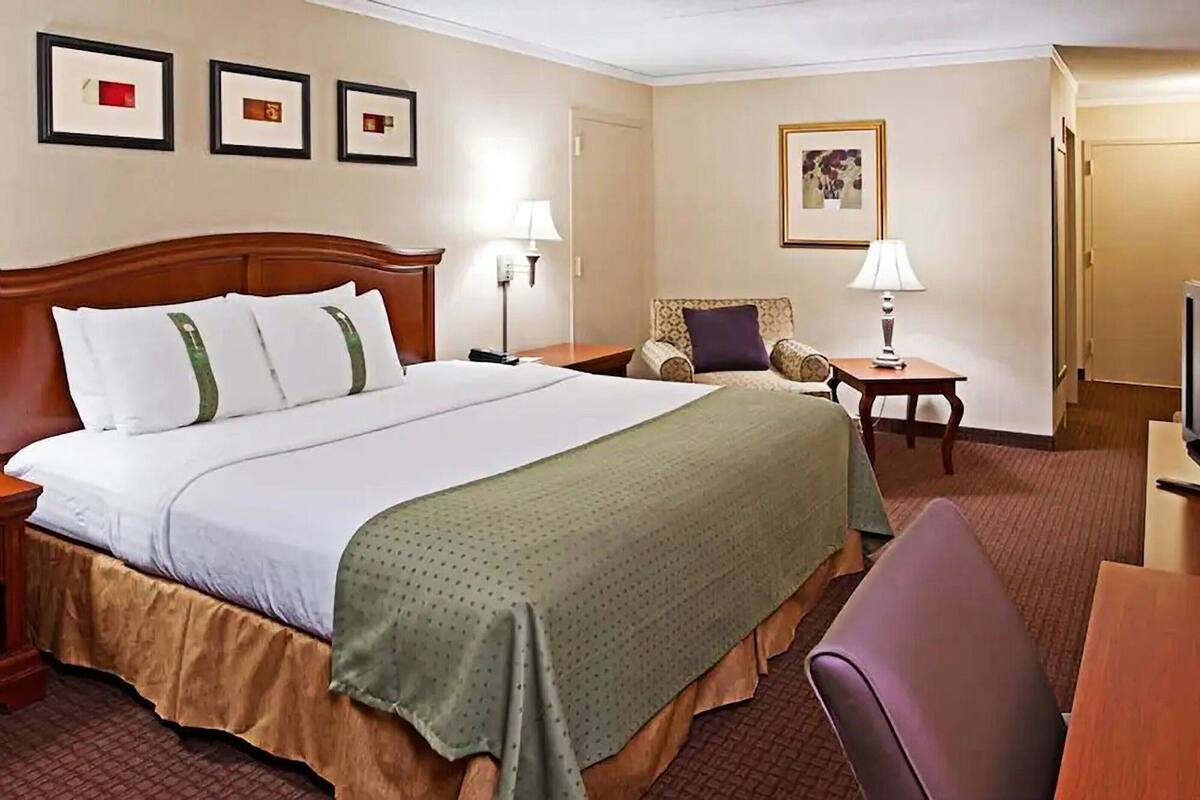 A hotel room with a large bed, two bedside tables, a chair, a desk, a television, and framed pictures on the wall.