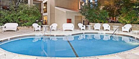 Una piscina interior con sillones blancos para tomar el sol y suelo de baldosas.