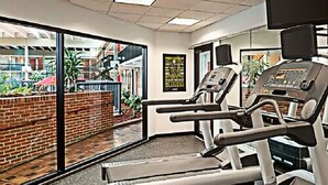 A gym with treadmills and exercise equipment, large windows, and a view of an outdoor area with plants and a brick wall. - Days Inn by Wyndham Warren (Warren)
