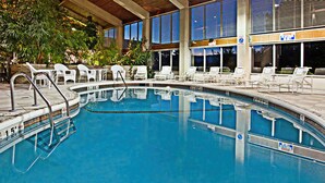An indoor swimming pool with clear water, surrounded by white lounge chairs and a covered area with large windows. - Days Inn by Wyndham Warren (Warren)