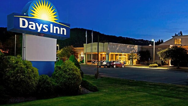 A Days Inn sign with a sun logo, a parking lot, and a building with a modern design.