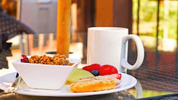 A breakfast setting with a bowl of granola, fresh fruits, and a pastry on a plate, accompanied by a white mug.
