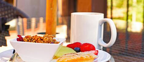 A breakfast setting with a bowl of granola, fresh fruits, and a pastry on a plate, accompanied by a white mug.