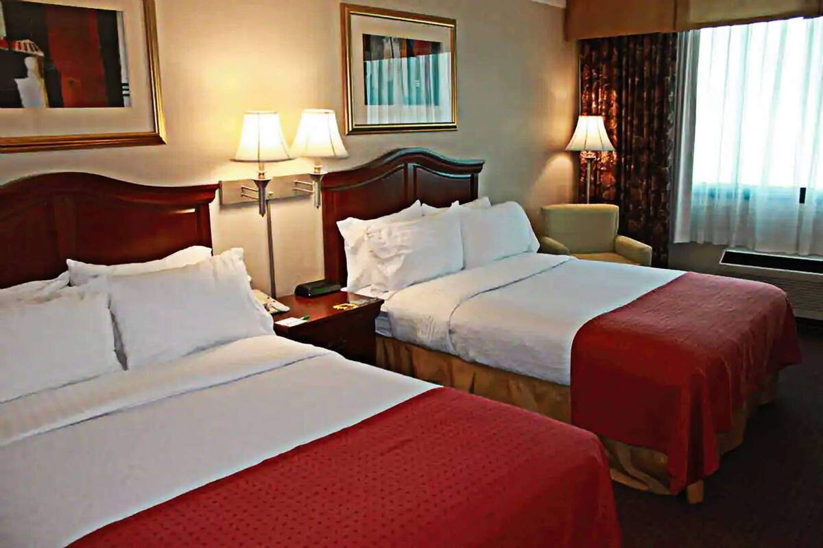 A hotel room with two beds, a nightstand, a chair, a lamp, and a window with curtains.
