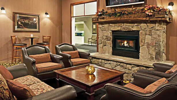 A cozy living room with leather sofas, a stone fireplace, and a flat-screen TV mounted above the fireplace. - Days Inn by Wyndham Warren (Warren)