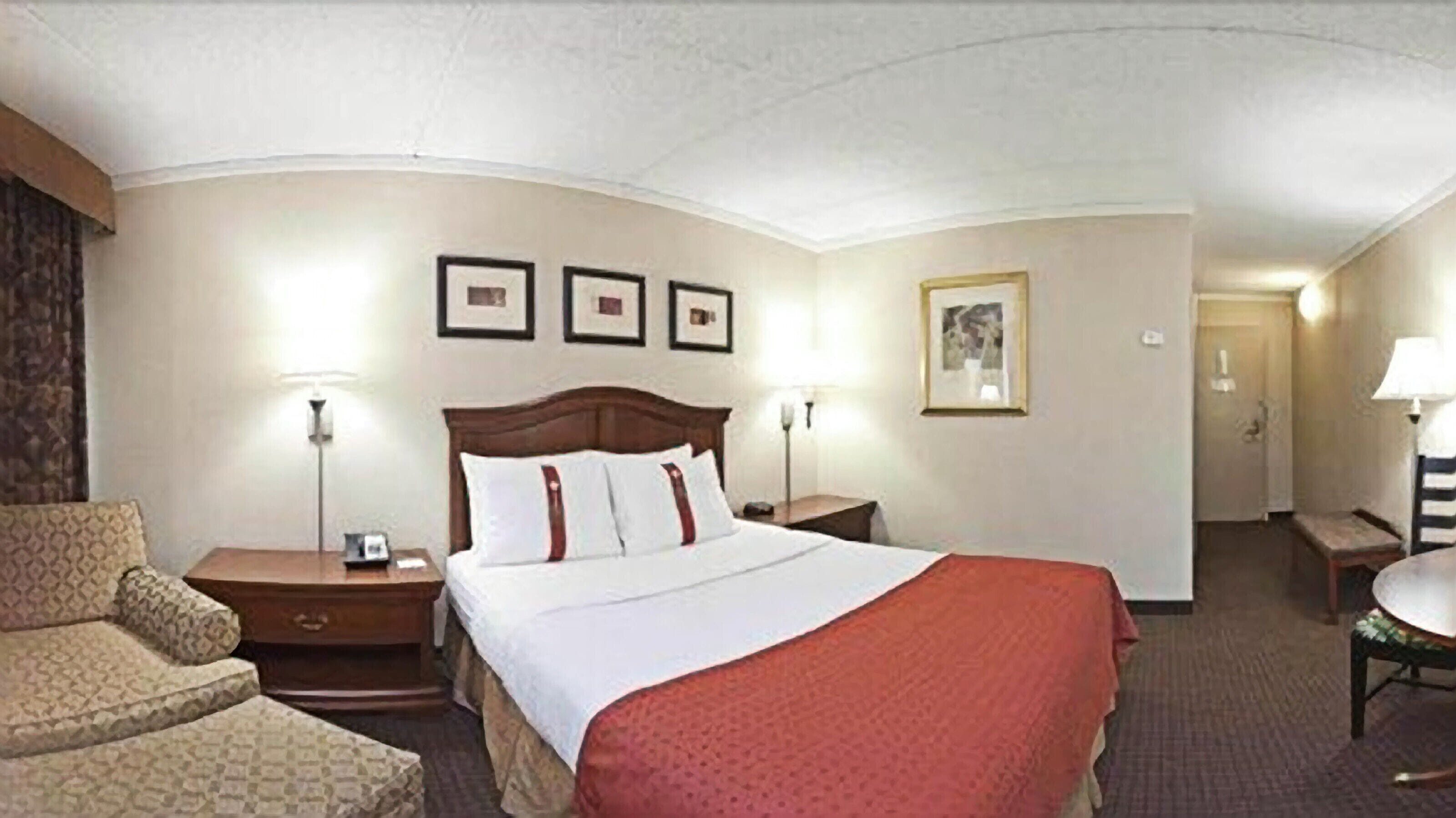 A hotel room with a large bed, two bedside tables, a chair, a desk, and a lamp.