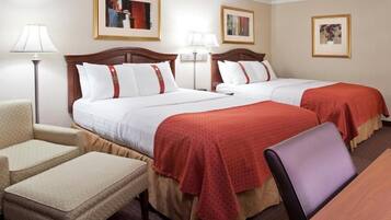 A hotel room with two beds, a desk, a chair, and a lamp.
