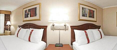 A hotel room with two beds, a nightstand, a lamp, and two framed pictures on the walls.