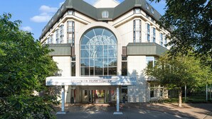 A large, historic building with a prominent arched glass window and a modern entrance. - Leonardo Hotel Weimar (Weimar)