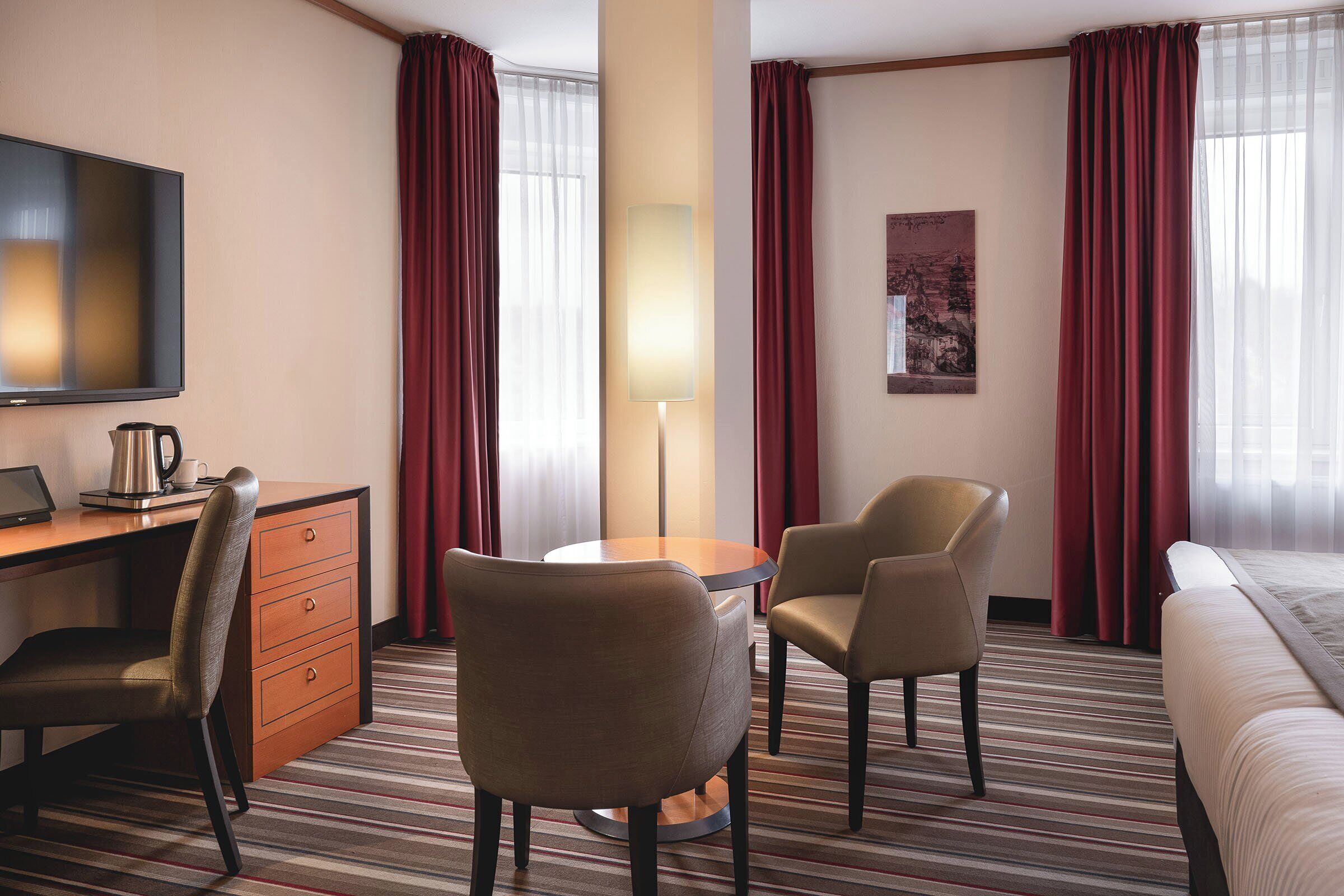 Una habitación de hotel con una cama, un escritorio con una computadora portátil, dos sillas, una lámpara y un televisor.