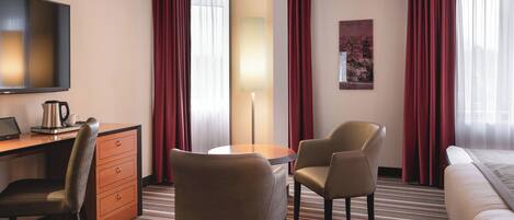 A hotel room with a bed, a desk with a laptop, two chairs, a lamp, and a TV.