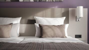 A neatly made bed with white and brown pillows, a striped blanket, and a wall-mounted light fixture.