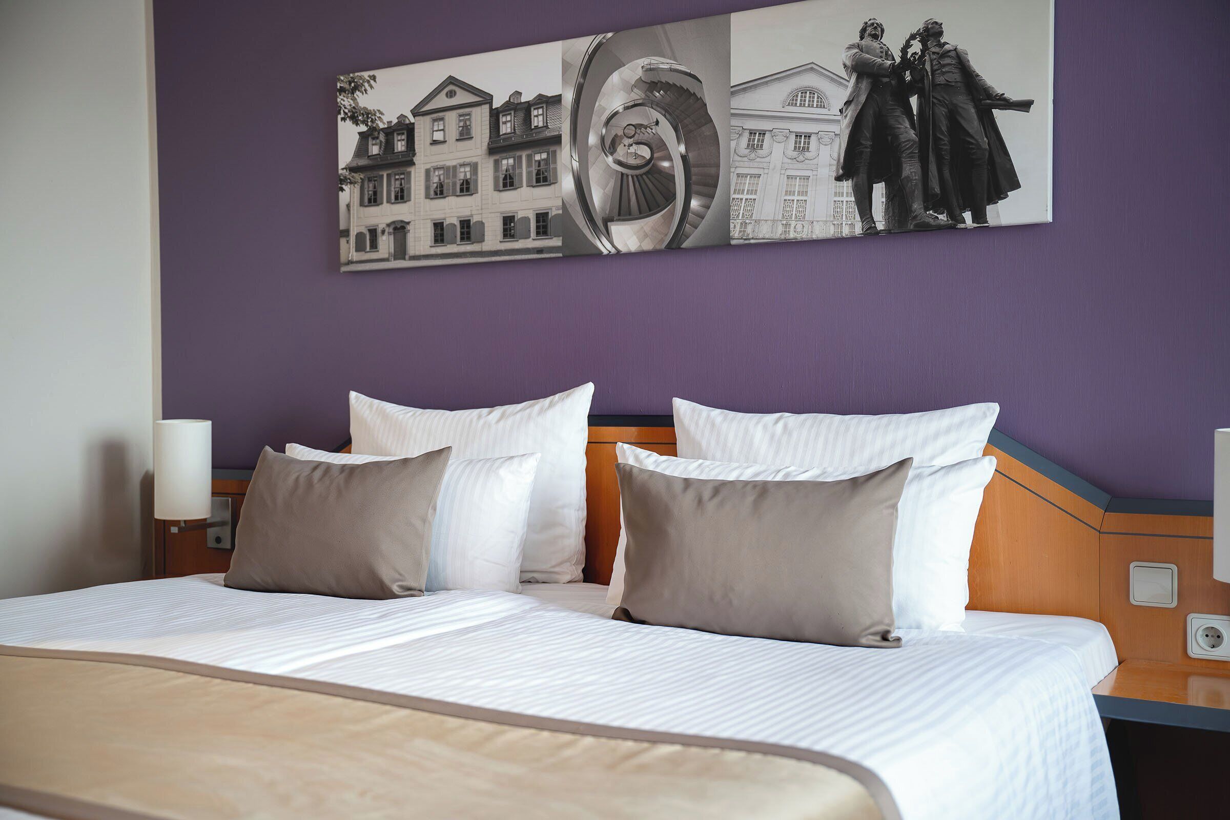 A double bed with white and beige bedding, a headboard with a wooden panel, and a wall-mounted artwork depicting a building and a statue.