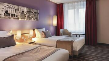A hotel room with two beds, a desk, a chair, a lamp, and a large window with curtains.