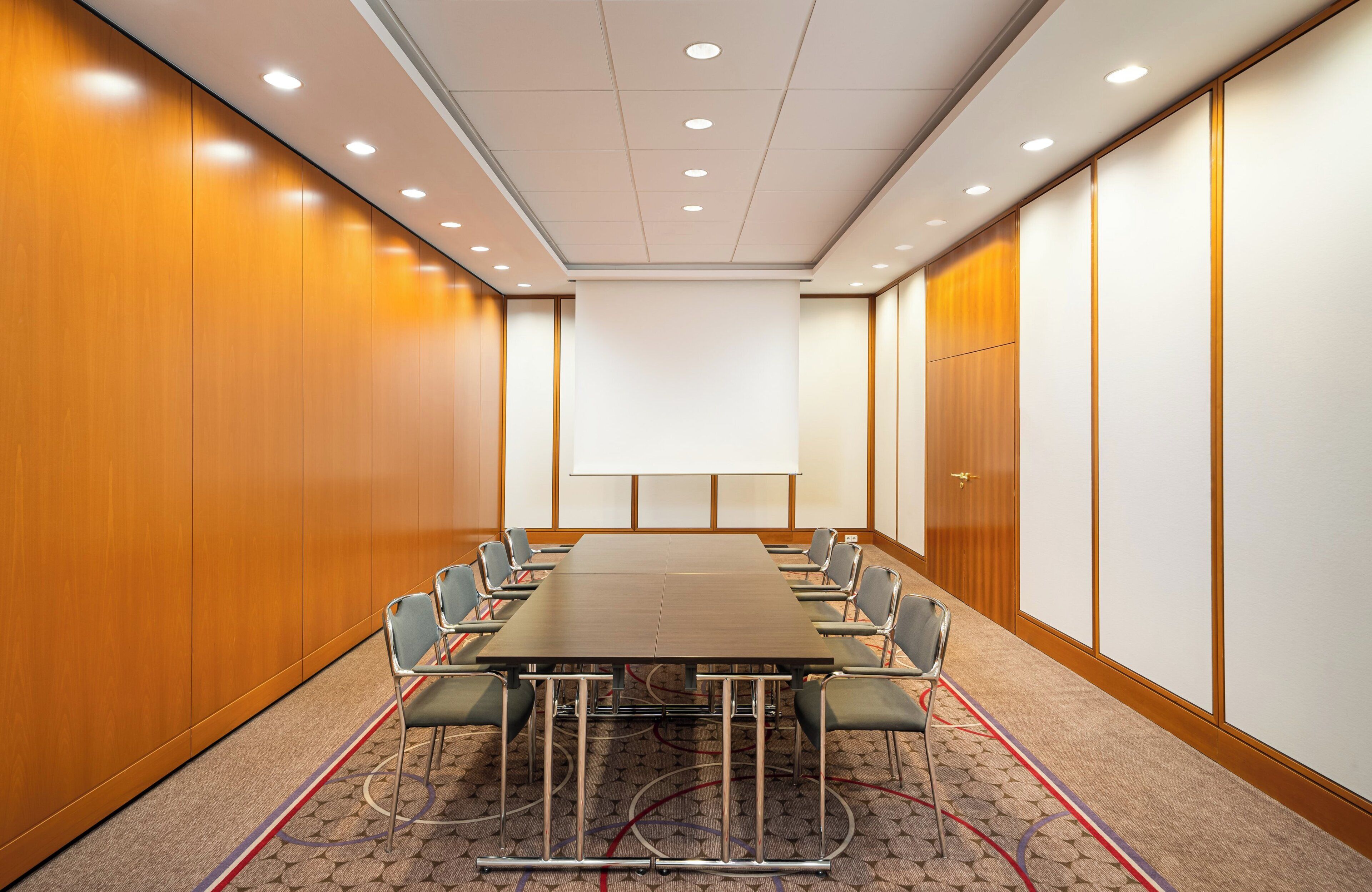 A conference room with a long table, chairs, and a projector screen.