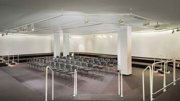 Ein Konferenzraum mit Reihen von Stühlen, einer Bühne inklusive Beleuchtung und einer hohen Decke.