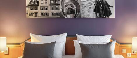 A hotel room with a bed, two bedside lamps, and a large framed artwork above the bed.