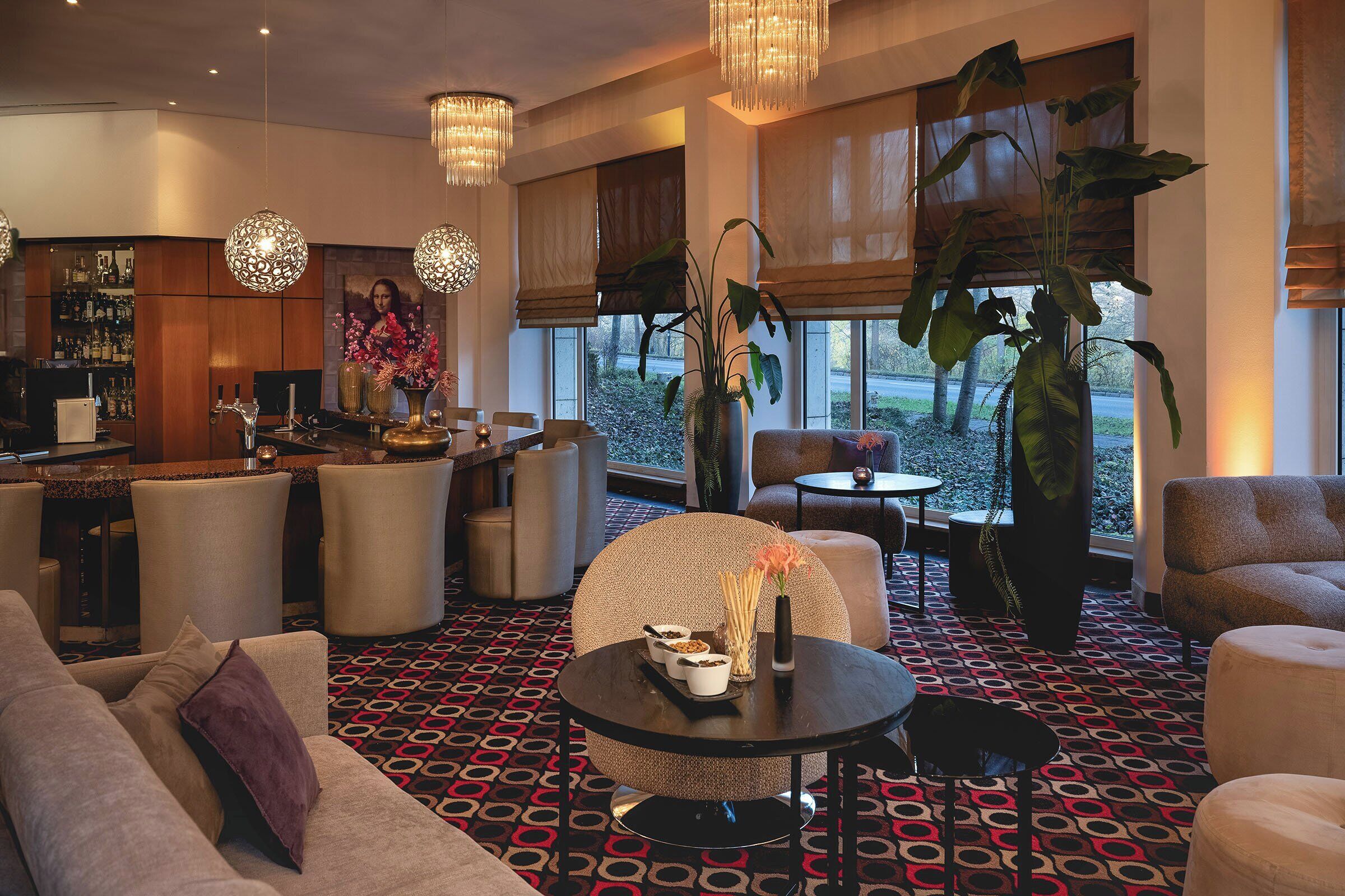 Un moderno vestíbulo de hotel con área de bar, zonas de estar y grandes ventanales que ofrecen vistas al exterior.