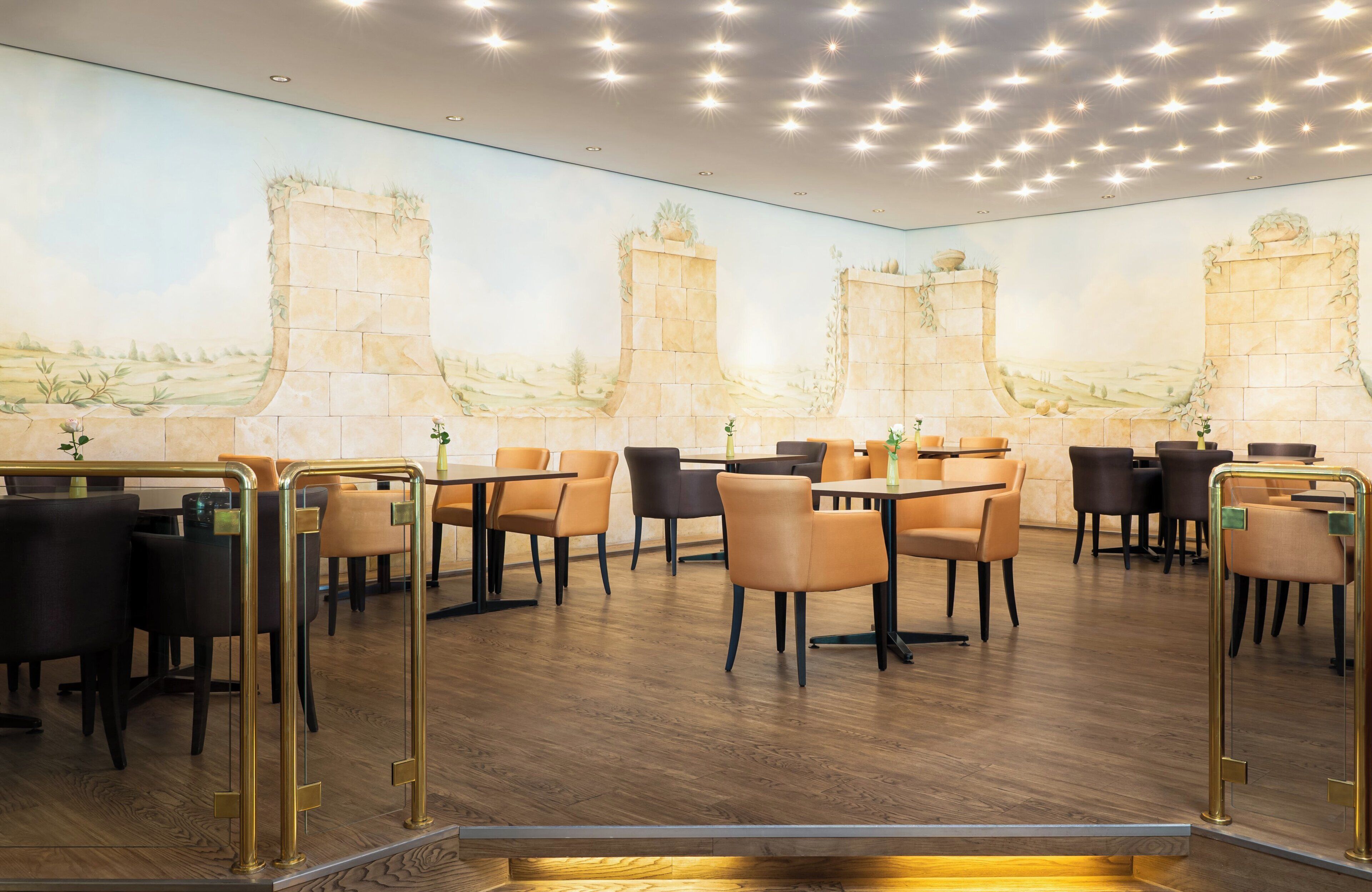 A restaurant with a mural of a castle on the wall, wooden flooring, and a variety of seating options including tables and chairs.