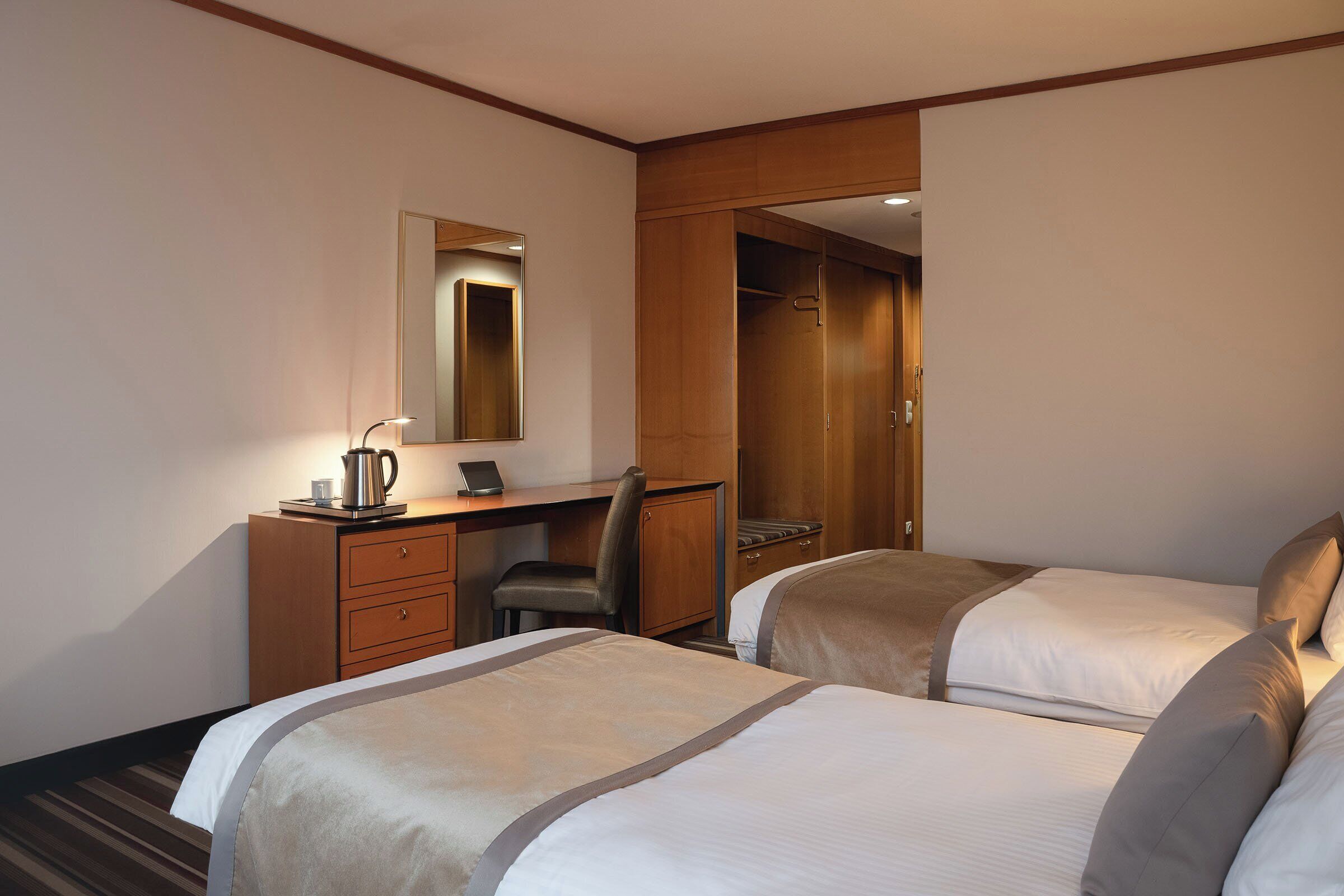 Habitación de hotel con dos camas, un escritorio con silla, un espejo y un armario.
