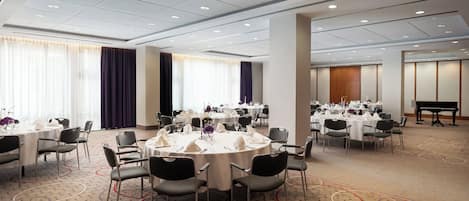 A conference room with round tables, chairs, and a piano.