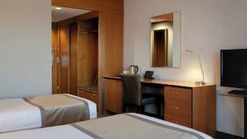 Quarto de hotel com duas camas, uma escrivaninha, uma cadeira, uma televisão e um guarda-roupa.