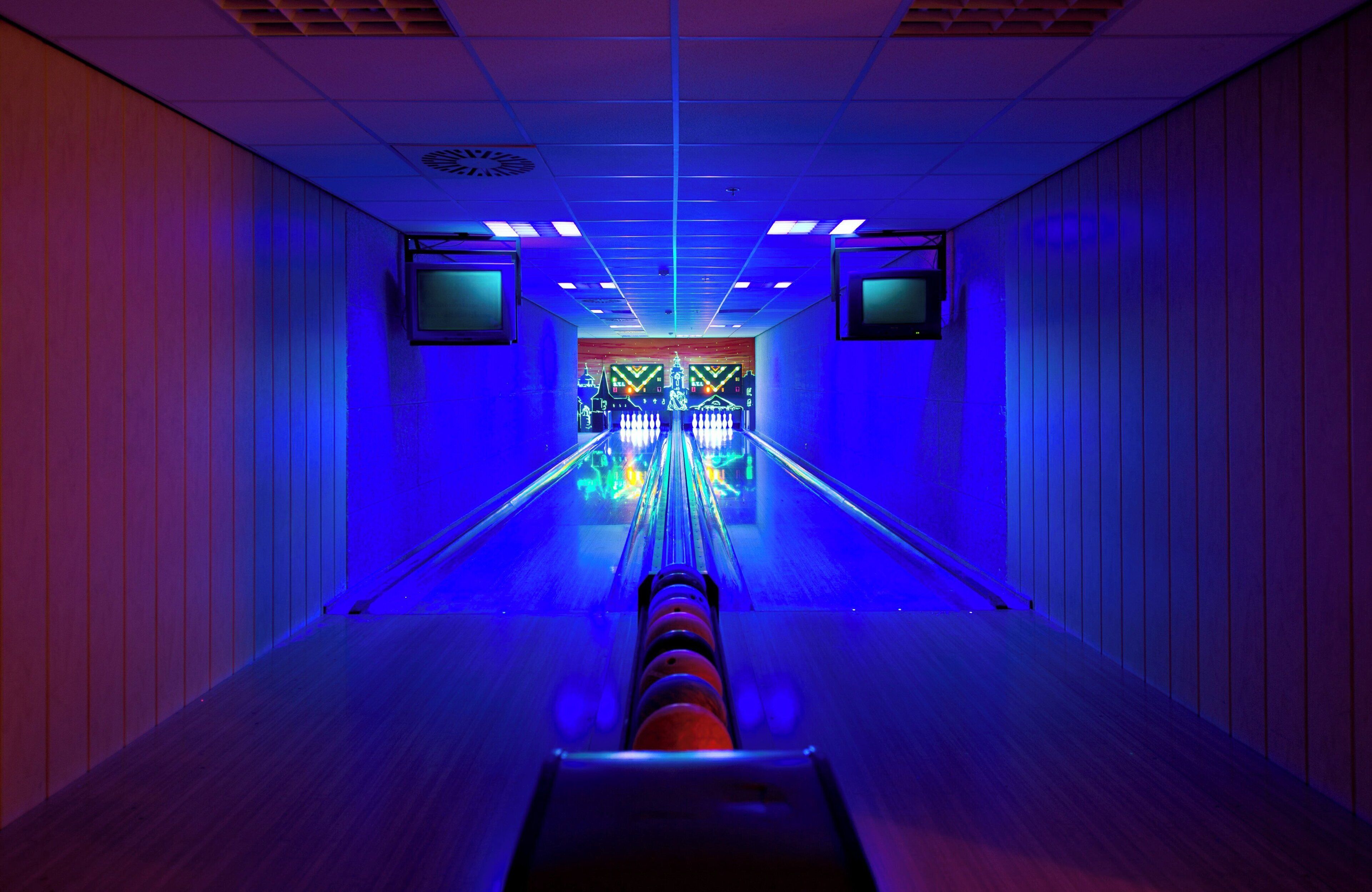 A bowling alley with a neon-lit lane and a colorful bowling ball return system.