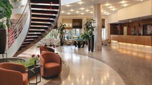 A modern lobby with a spiral staircase, seating area, reception desk, and large windows. - Leonardo Hotel Weimar (Weimar)