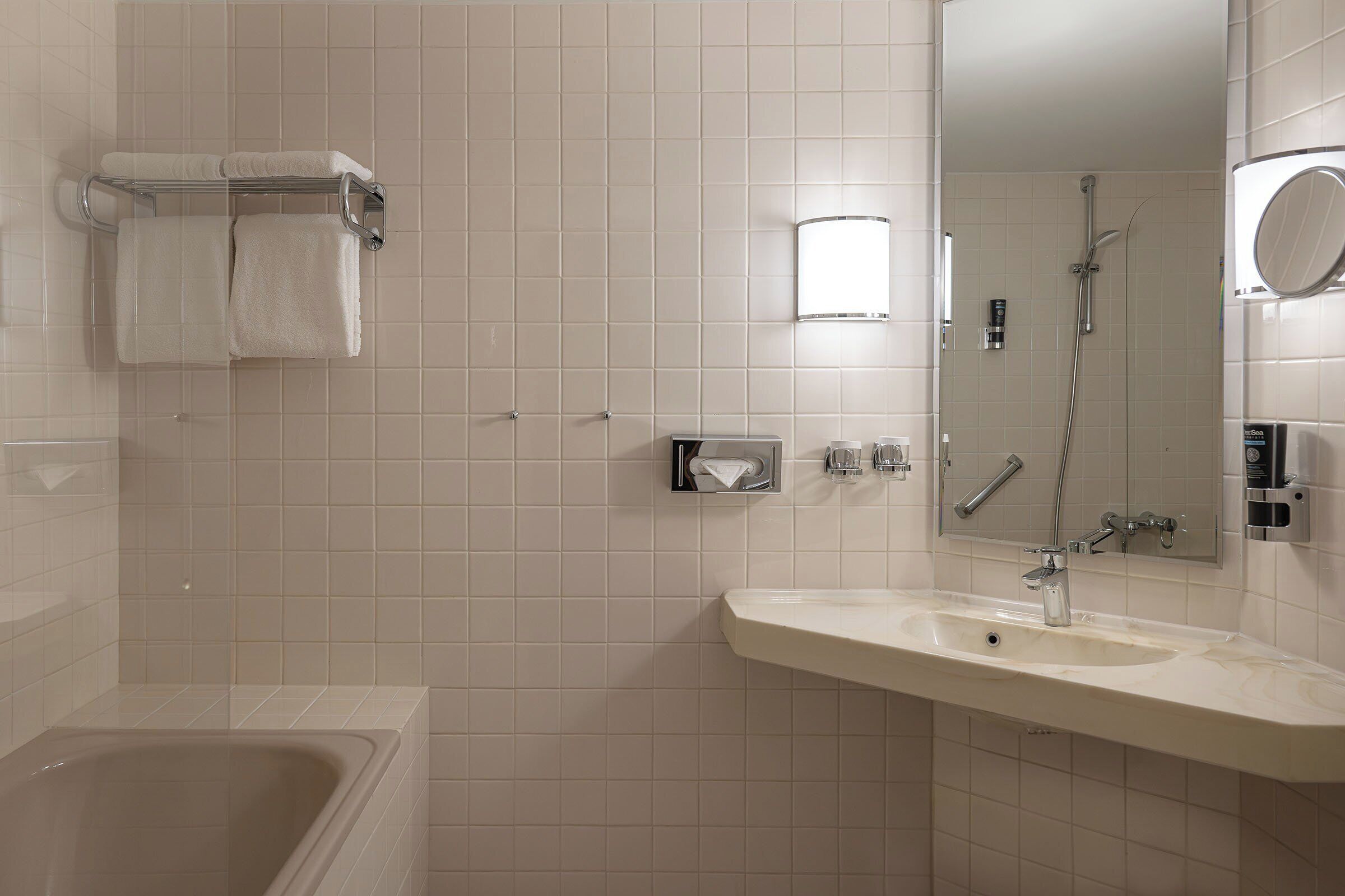 A modern bathroom with a bathtub, a sink, a mirror, and a towel rack.