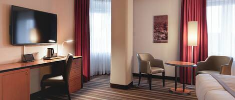 Habitación de hotel con cama, escritorio con computadora portátil, silla, mesa pequeña, televisor y lámpara.