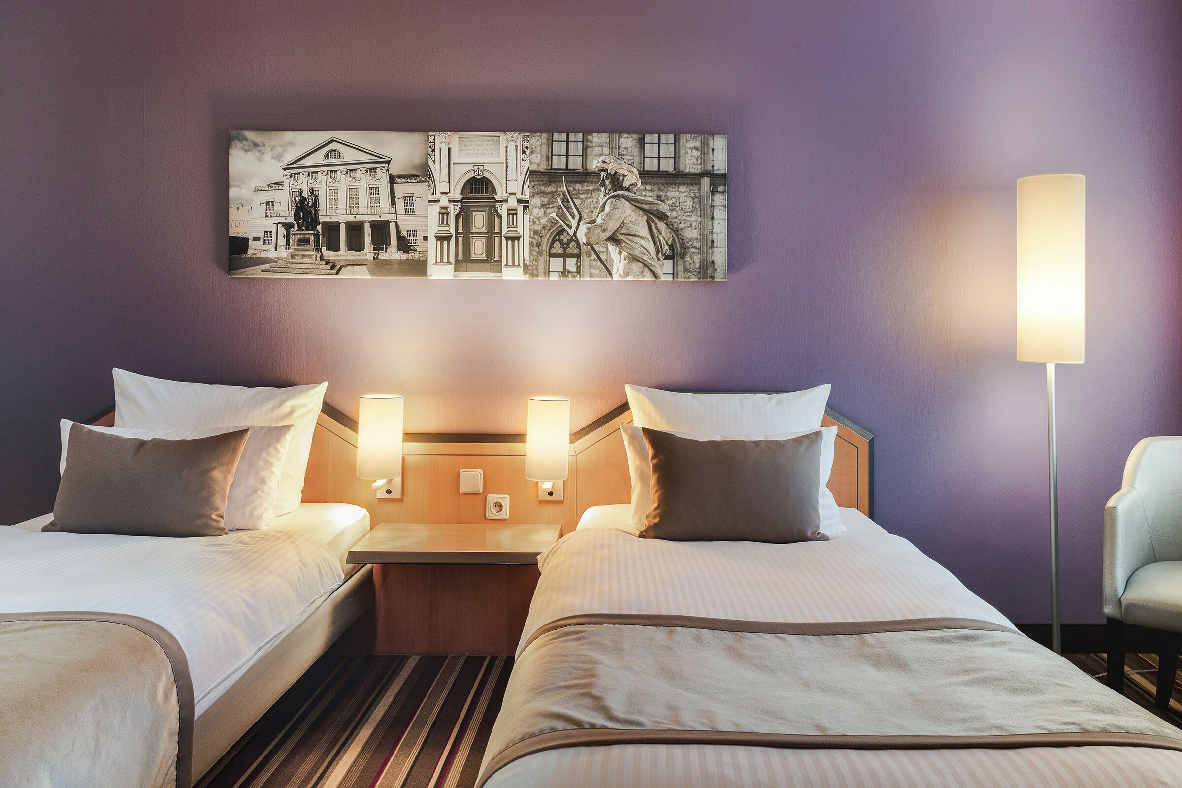 A hotel room with two beds, a nightstand, a lamp, and a wall-mounted artwork.